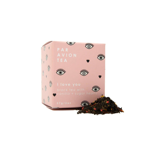 Pink tea box with decorative patterns and text, accompanied by a pile of black tea leaves on a white background.