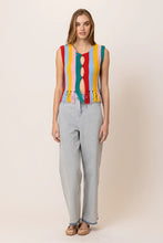 Load image into Gallery viewer, Model wearing a colorful striped knit tank top featuring vibrant vertical rainbow stripes, sleeveless design, fringe hem detailing, and functional front buttons; paired with light-wash drawstring jeans for a fun, retro-inspired summer look. Ideal for festivals and warm-weather style.
