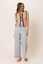 Load image into Gallery viewer, Model wearing a colorful striped knit tank top featuring vibrant vertical rainbow stripes, sleeveless design, fringe hem detailing, and functional front buttons; paired with light-wash drawstring jeans for a fun, retro-inspired summer look. Ideal for festivals and warm-weather style.

