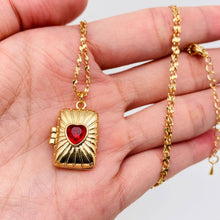 Load image into Gallery viewer, 14K gold-plated rectangular locket necklace with a red heart-shaped stone and radiating etched design on a delicate gold chain.
