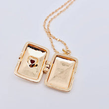 Load image into Gallery viewer, 14K gold-plated rectangular locket necklace with a red heart-shaped stone and radiating etched design on a delicate gold chain.
