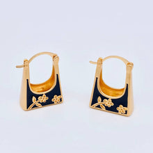 Load image into Gallery viewer, Black enamel handbag-shaped huggie earrings with gold-tone trim and delicate carved floral details.
