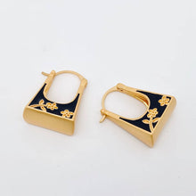 Load image into Gallery viewer, Black enamel handbag-shaped huggie earrings with gold-tone trim and delicate carved floral details.

