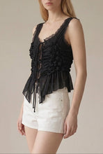 Load image into Gallery viewer, Model wearing a black sleeveless ruched lace tie top with intricate front ruching, lace trim and adjustable tie front paired with white shorts.
