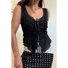 Load image into Gallery viewer, Model wearing a black sleeveless ruched lace tie top with intricate front ruching, lace trim and adjustable tie front paired with a polka dot skirt.
