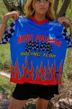 Load image into Gallery viewer, Woman wearing the All American Racing Team oversized mesh jersey featuring blue racing graphics, checkered sleeves, flame details, varsity lettering, and a large number 76 on the back.
