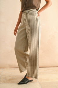 Person wearing striped pants and a brown top against a beige background