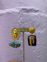 Load image into Gallery viewer, Gold asymmetrical statement earrings featuring sculptural abstract details with turquoise enamel, black enamel, textured gold accents, and an artistic modern design displayed on a jewelry stand.
