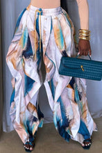 Load image into Gallery viewer, Model wearing abstract marble print draped wide-leg pants in blue, ivory, blush, and sand tones with layered flowing panels, styled with gold bangles and a teal handbag.
