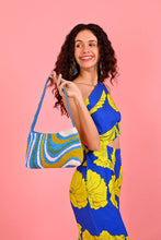 Load image into Gallery viewer, Woman in a blue and yellow dress holding a colorful bag against a pink background
