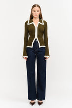Load image into Gallery viewer, Model wearing olive green fitted double-zip knit top with ivory fuzzy trim, long sleeves, and pointed collar, styled with dark-wash wide-leg jeans.”
