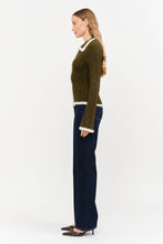 Load image into Gallery viewer, Model wearing olive green fitted double-zip knit top with ivory fuzzy trim, long sleeves, and pointed collar, styled with dark-wash wide-leg jeans.”
