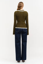 Load image into Gallery viewer, Model wearing olive green fitted double-zip knit top with ivory fuzzy trim, long sleeves, and pointed collar, styled with dark-wash wide-leg jeans.”
