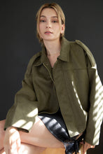 Load image into Gallery viewer, Woman wearing an olive green jacket sitting against a dark background
