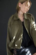 Load image into Gallery viewer, Woman wearing an olive green jacket against a dark background
