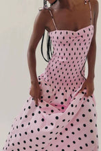Load image into Gallery viewer, Pink polka dot midi dress with a smocked bodice, thin straps, and a flowy skirt, worn by a model.
