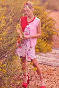 Woman in a floral dress and red  & Pink cardigan sweater vest top standing among yellow flowers.
