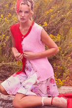 Load image into Gallery viewer, Woman in a pink &amp; red sleeveless cardigan vest top and floral dress sitting outdoors with flowers in the background
