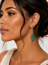 Load image into Gallery viewer, A close-up of a woman wearing a dangling earring with a pink rectangular stone, a small white pearl-like chain, and a larger teal marquise-shaped drop set in gold.
