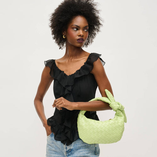 Woman holding a pistachio green woven handbag against a plain background