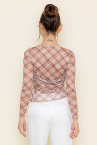 Person wearing a plaid long-sleeve top and white pants against a beige background