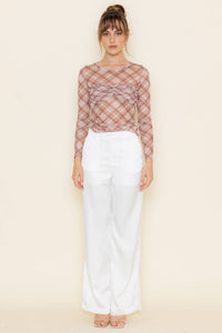 Woman wearing a sheer plaid top and white pants on a beige background
