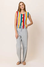 Load image into Gallery viewer, Model wearing a colorful striped knit tank top featuring vibrant vertical rainbow stripes, sleeveless design, fringe hem detailing, and functional front buttons; paired with light-wash drawstring jeans for a fun, retro-inspired summer look. Ideal for festivals and warm-weather style.
