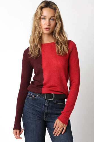 Woman wearing a red and burgundy sweater with blue jeans on a white background
