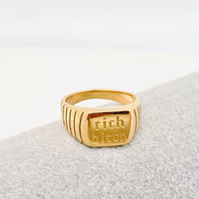 Load image into Gallery viewer, Chunky 18K gold-plated signet ring engraved with “rich bitch” and featuring ribbed detailing along the sides.
