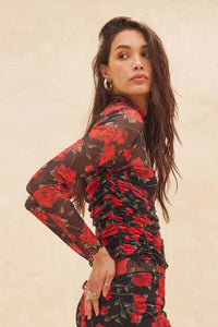 Woman wearing a black skirt & matching top with red floral patterns against a beige background