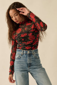 Person wearing Glam Expressway's red and black floral long-sleeve bodysuit top with blue jeans on a beige background