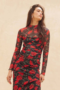 Woman wearing a black skirt and matching top with red floral pattern against a beige background