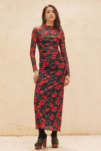 Woman wearing a black skirt and matvhing bodysuit with red floral pattern against a beige background