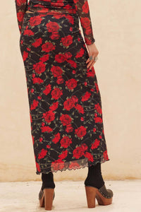 Long black skirt with red floral pattern worn by a person on a beige background