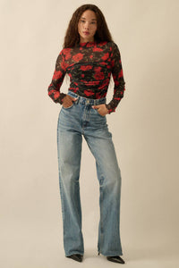 Woman wearing Glam Expressway's red and black floral top with blue jeans on a beige background