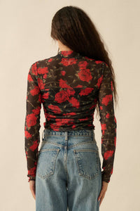 Person wearing a long-sleeve top with red floral pattern and blue jeans on a beige background