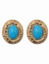 Load image into Gallery viewer, Oversized gold statement stud earrings with oval turquoise stone center and textured hammered gold frame on white background.


