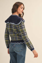 Load image into Gallery viewer, Model wearing a ruffled plaid knit cardigan with puff sleeves, scalloped trim, button-front V neckline, and contrast cable-knit yoke, styled with denim jeans.
