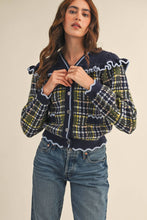 Load image into Gallery viewer, Model wearing a ruffled plaid knit cardigan with puff sleeves, scalloped trim, button-front V neckline, and contrast cable-knit yoke, styled with denim jeans.
