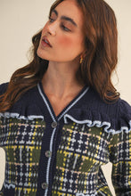 Load image into Gallery viewer, Model wearing a ruffled plaid knit cardigan with puff sleeves, scalloped trim, button-front V neckline, and contrast cable-knit yoke, styled with denim jeans.
