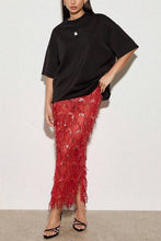 Load image into Gallery viewer, Model wearing a vibrant red sequin fringe midi skirt featuring intricate embellishments and textured tassel detailing paired with an oversized black t-shirt.
