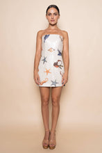 Load image into Gallery viewer, Model wearing a strapless white sequin mini dress featuring ocean-inspired seashell, starfish, and seahorse embellishments in a fitted bodycon silhouette.

