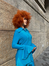Load image into Gallery viewer, Person wearing a blue outfit with red hair lying on a concrete surface.
