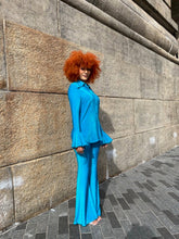 Load image into Gallery viewer, Person wearing a blue outfit lying on stone steps with a gray wall background
