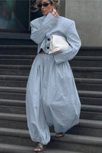 Load image into Gallery viewer, A woman stands on outdoor concrete stairs wearing a light blue oversized two-piece outfit with a cropped jacket and matching loose pants, holding a white clutch.
