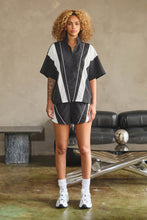 Load image into Gallery viewer, Black oversized half-zip nylon top with white mesh contrast panels, mock neckline, white piping, short sleeves, and adjustable drawcord hem.
