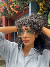 Load image into Gallery viewer, Model wearing oversized square green sunglasses with transparent frames and tinted lenses, posing in front of Glam Expressway Boutique in DUMBO, Brooklyn. Trendy summer eyewear offering UV protection and bold retro style.
