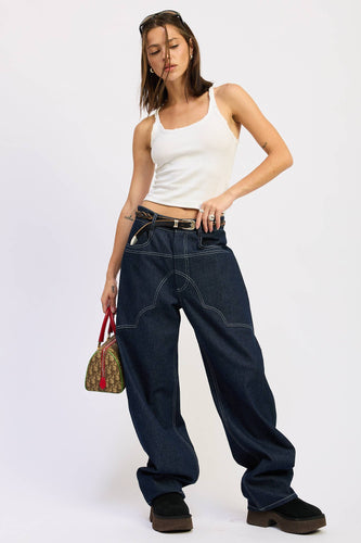 Woman wearing a white tank top and dark blue jeans, holding a colorful handbag on a white background
