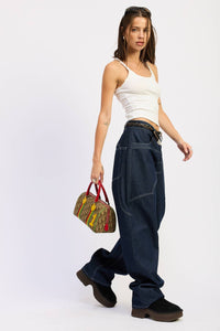 Woman wearing a white tank top and dark blue jeans, holding a colorful bag on a white background