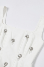 Load image into Gallery viewer, White structured bustier top featuring wide straps and multiple crystal floral embellishments across the front, photographed on a white background.
